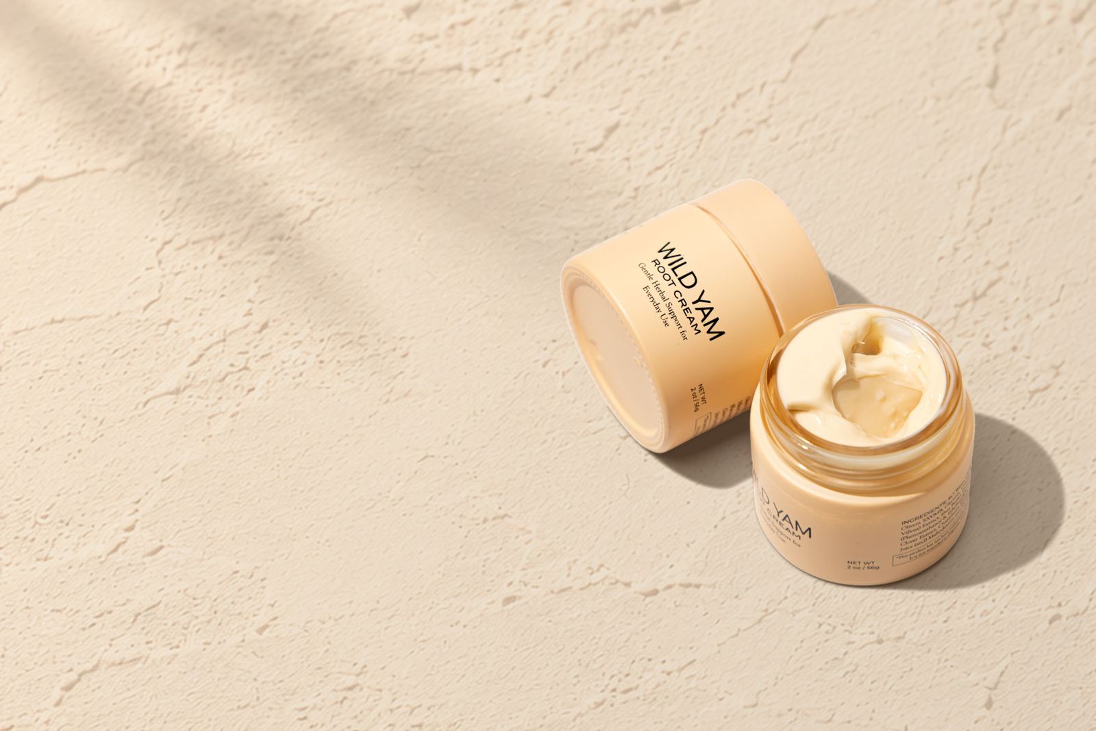 Two jars of Weed & Root Wild Yam Root Cream, one open, on a sunlit plaster surface